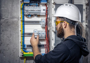 Male electrician at the checkout counter on a blurred background of a switchboard.